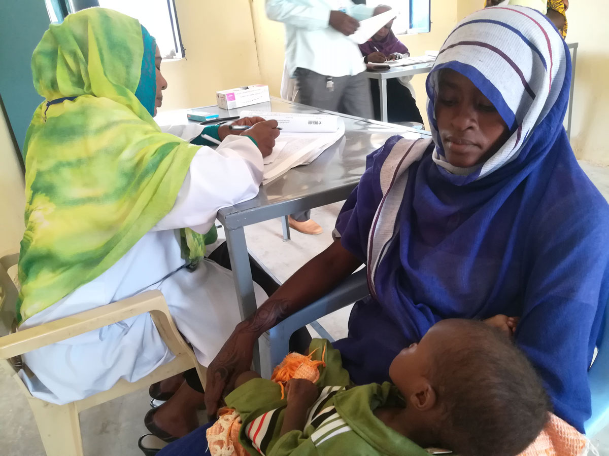 Aziza, 24, holds her young son, Adam, in her arms during his weekly checkup at Relief International's clinic in Zamzam A.