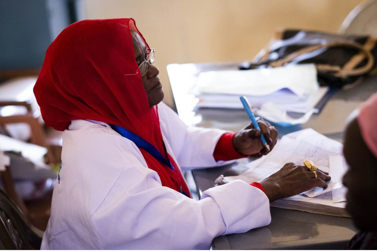 A female Relief International healthcare staff member sat at her desk with a pen in her hand